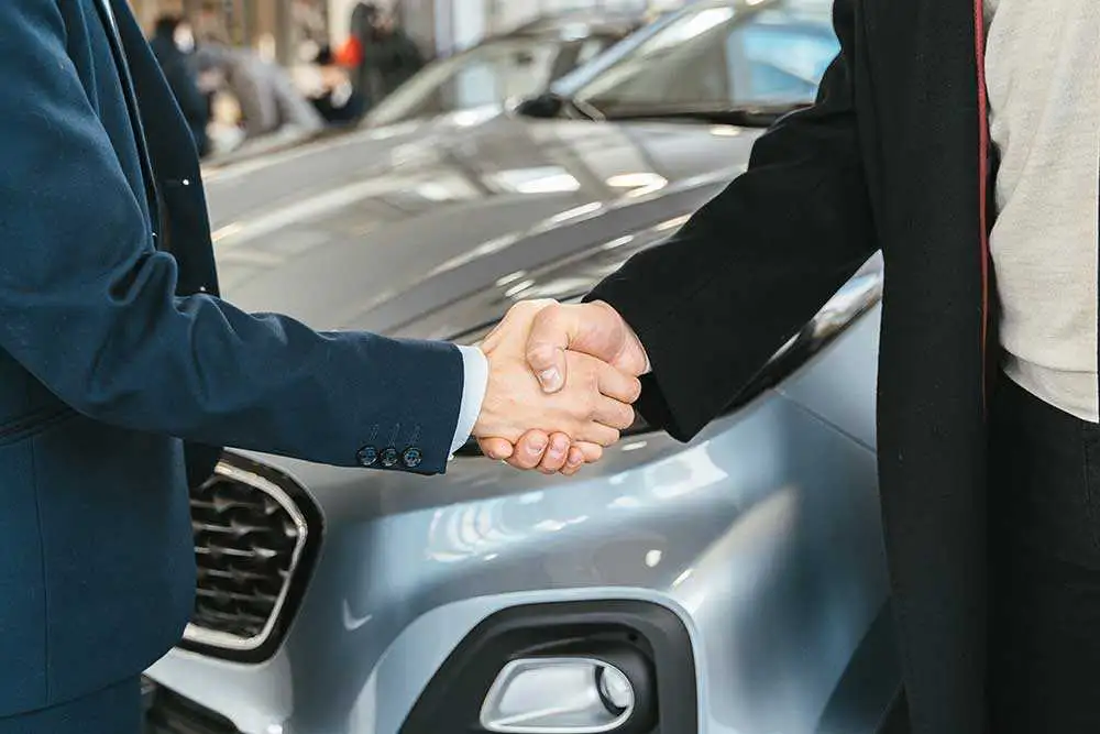 Autokaufvertrag online: Käufer und Verkäufer geben sich vor dem Auto die Hand