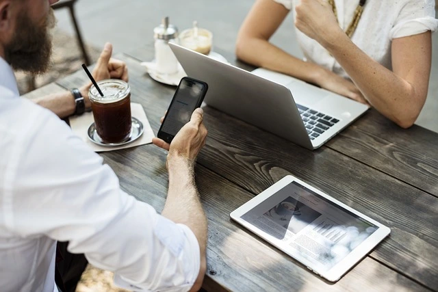 Autokaufvertrag online nutzen Zwei Personen nutzen Laptop und Handy bei der Erstellung eines Autokaufvertrags online, Kaffee auf dem Tisch